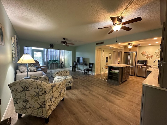 living room featuring wood-type flooring, a textured ceiling, and ceiling fan