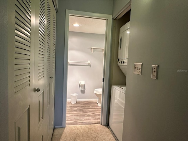 interior space with a textured ceiling, toilet, wood-type flooring, and stacked washer and dryer