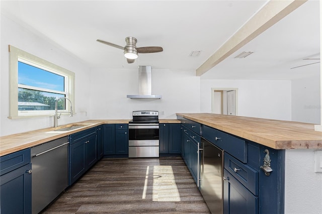 kitchen with blue cabinets, sink, wall chimney exhaust hood, appliances with stainless steel finishes, and butcher block countertops