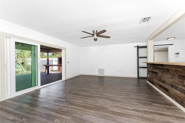 unfurnished living room featuring a barn door, ceiling fan, and dark wood-type flooring