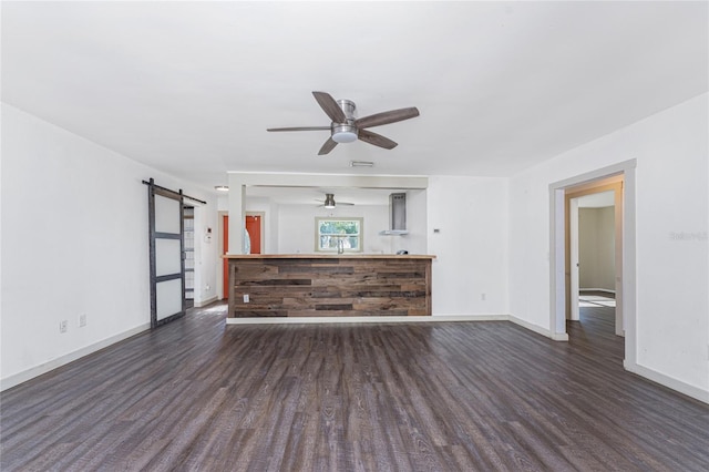 unfurnished living room with dark hardwood / wood-style floors, a barn door, and ceiling fan