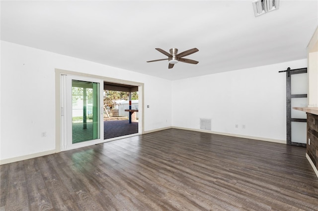 unfurnished living room featuring a barn door, ceiling fan, and dark wood-type flooring