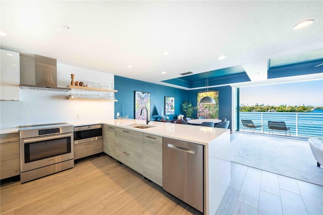 kitchen featuring wall chimney range hood, hanging light fixtures, sink, appliances with stainless steel finishes, and kitchen peninsula