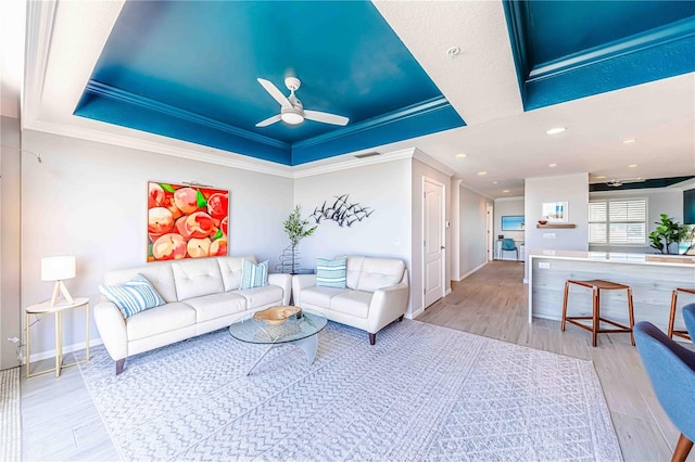 living room featuring ceiling fan, light hardwood / wood-style floors, a raised ceiling, and crown molding