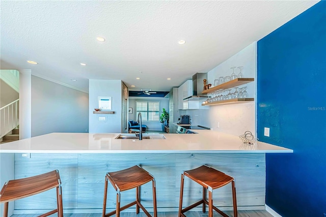 kitchen featuring a kitchen bar, kitchen peninsula, light hardwood / wood-style flooring, and wall chimney range hood