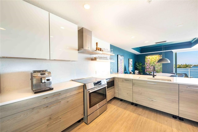 kitchen featuring sink, hanging light fixtures, electric range, wall chimney exhaust hood, and light wood-type flooring