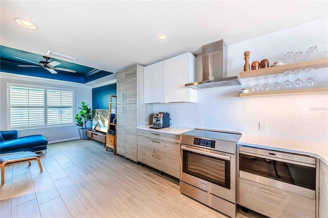 kitchen featuring white cabinetry, wall chimney range hood, light hardwood / wood-style floors, a tray ceiling, and stainless steel stove