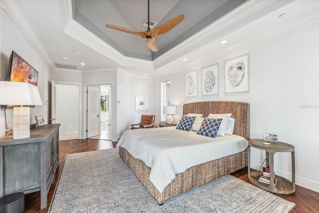 bedroom featuring a raised ceiling, crown molding, ensuite bath, ceiling fan, and dark hardwood / wood-style flooring