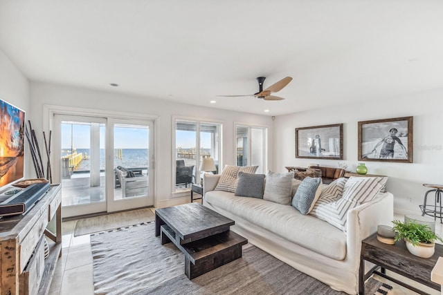 living room with ceiling fan, a water view, and light wood-type flooring