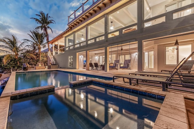 pool at dusk featuring a patio area and an in ground hot tub