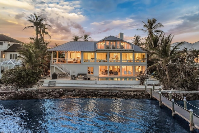 back house at dusk featuring a balcony, a pool, a patio area, and a water view