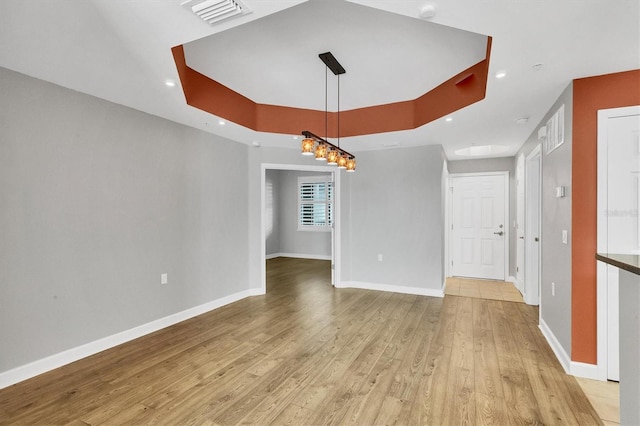 unfurnished dining area with a tray ceiling and light hardwood / wood-style flooring