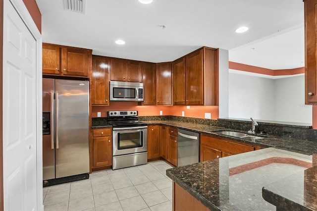 kitchen with kitchen peninsula, stainless steel appliances, dark stone counters, light tile patterned flooring, and sink