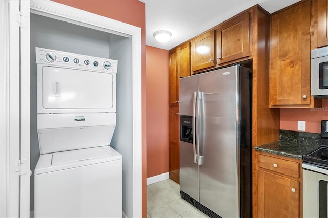 kitchen featuring stacked washer and dryer, stainless steel fridge with ice dispenser, dark stone countertops, electric range, and light tile patterned flooring