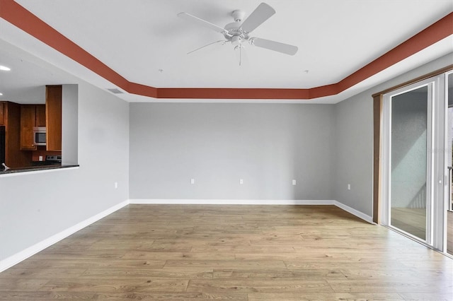 spare room featuring a raised ceiling, light wood-type flooring, and ceiling fan