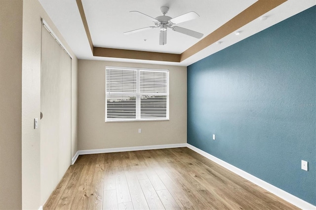 empty room with a raised ceiling, ceiling fan, and light wood-type flooring