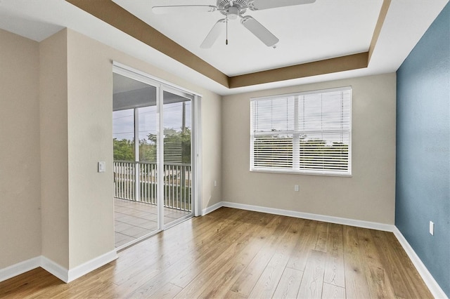 unfurnished room featuring a raised ceiling, ceiling fan, and light hardwood / wood-style floors