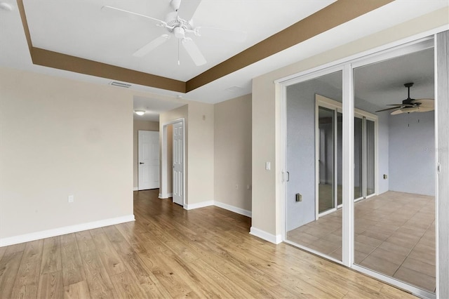 empty room with ceiling fan, light hardwood / wood-style floors, and a tray ceiling