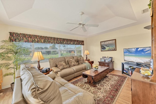 living room featuring a raised ceiling, ceiling fan, plenty of natural light, and light hardwood / wood-style floors