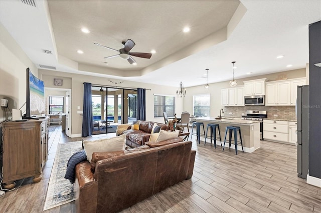 living room featuring light wood-type flooring, a tray ceiling, ceiling fan, and sink