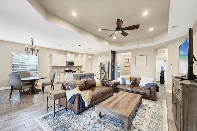 living room featuring a raised ceiling, sink, and ceiling fan with notable chandelier