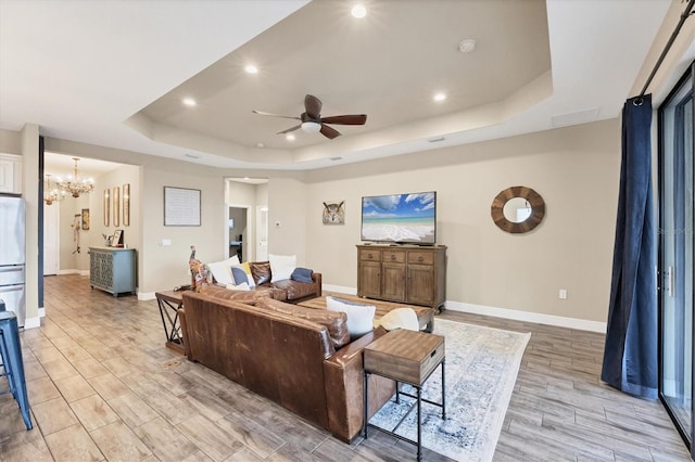 living room featuring ceiling fan with notable chandelier and a tray ceiling