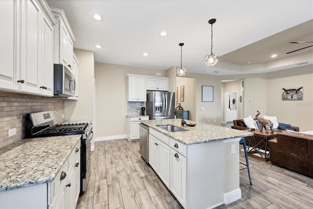 kitchen with a kitchen island with sink, hanging light fixtures, appliances with stainless steel finishes, light stone counters, and white cabinetry