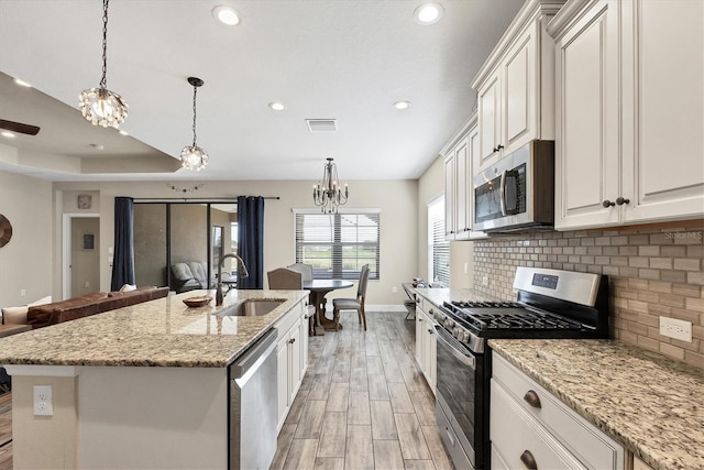 kitchen featuring a kitchen island with sink, white cabinets, hanging light fixtures, sink, and appliances with stainless steel finishes