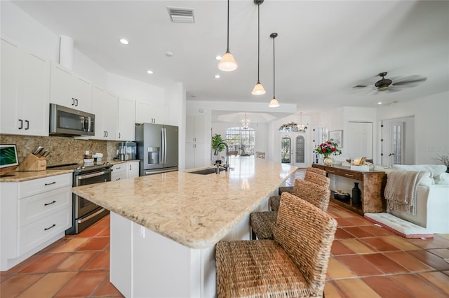 kitchen with appliances with stainless steel finishes, a kitchen island with sink, sink, pendant lighting, and white cabinets