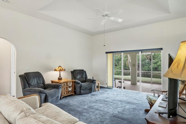 carpeted living room with ceiling fan and a tray ceiling