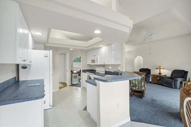 kitchen featuring a tray ceiling, kitchen peninsula, white cabinetry, and white appliances