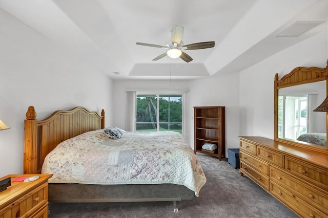 bedroom with a raised ceiling, ceiling fan, dark carpet, and access to outside