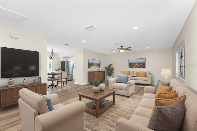 living room featuring ceiling fan with notable chandelier and light hardwood / wood-style floors