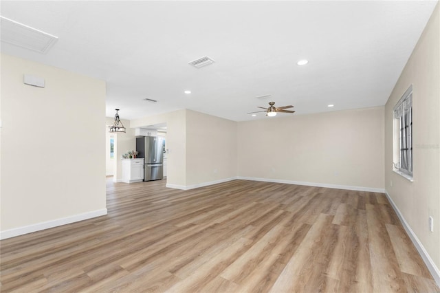 unfurnished living room featuring ceiling fan with notable chandelier and light hardwood / wood-style floors