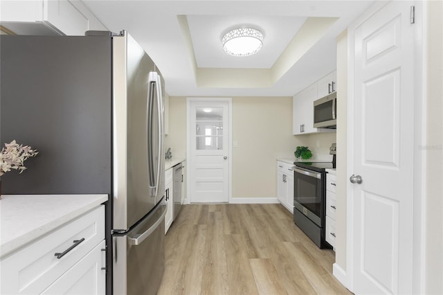 kitchen featuring a raised ceiling, white cabinetry, light hardwood / wood-style flooring, and appliances with stainless steel finishes