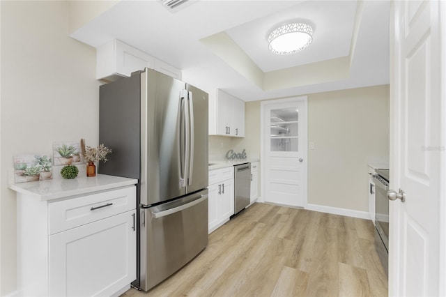 kitchen with appliances with stainless steel finishes, light hardwood / wood-style flooring, white cabinetry, and a raised ceiling