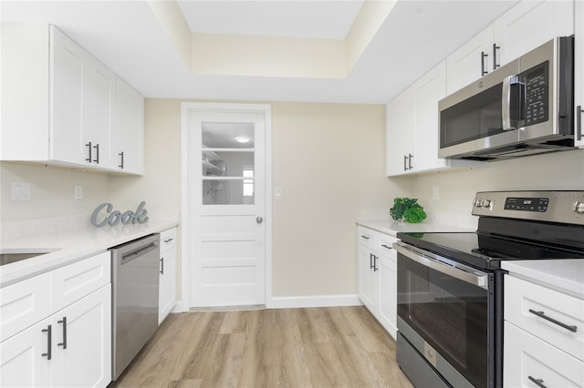 kitchen featuring light hardwood / wood-style floors, a raised ceiling, white cabinetry, and appliances with stainless steel finishes