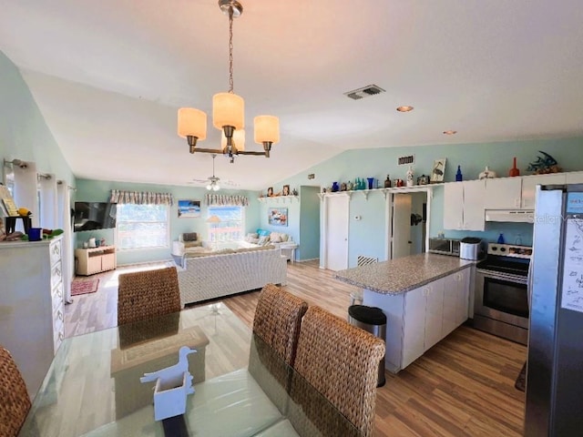 dining room with ceiling fan with notable chandelier, light hardwood / wood-style flooring, and lofted ceiling