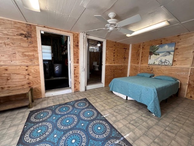 bedroom with wood walls, connected bathroom, a ceiling fan, and tile patterned floors