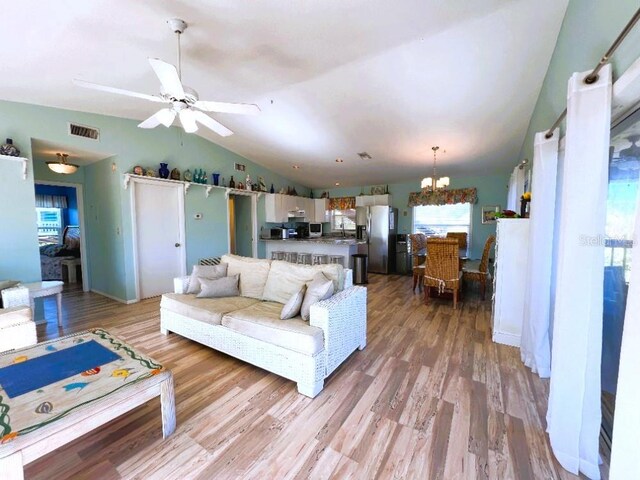 living area with light wood-type flooring, visible vents, vaulted ceiling, and ceiling fan with notable chandelier