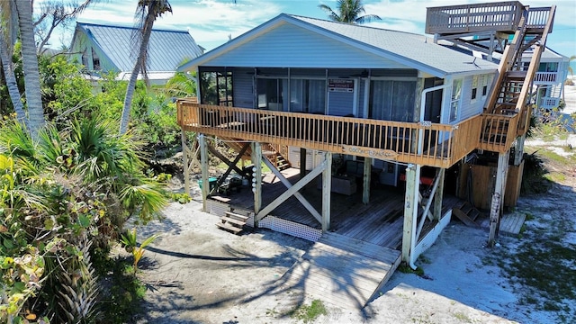 rear view of property featuring roof with shingles, stairway, a wooden deck, and a sunroom