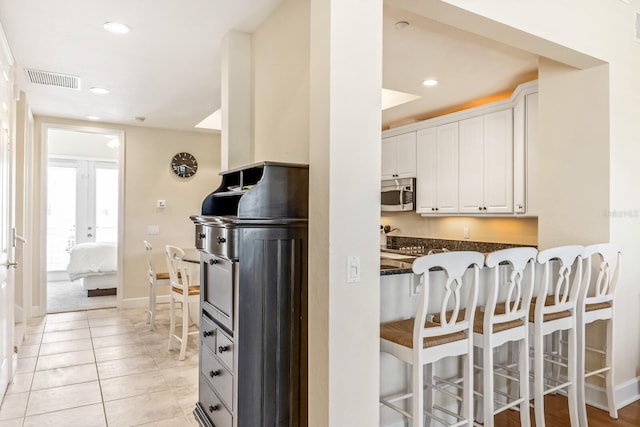 kitchen with dark stone counters, french doors, a kitchen breakfast bar, light tile patterned floors, and white cabinetry