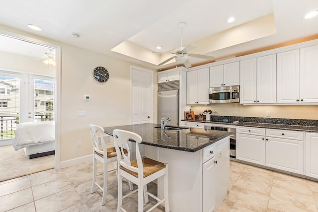 kitchen with stainless steel appliances, sink, dark stone countertops, white cabinets, and an island with sink