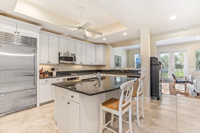 kitchen with white cabinets, a raised ceiling, ceiling fan, dark stone countertops, and stainless steel appliances