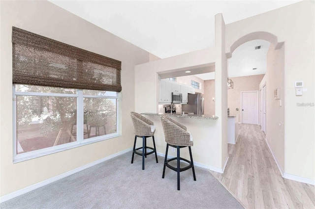 kitchen with white cabinetry, a kitchen breakfast bar, stainless steel appliances, kitchen peninsula, and light stone countertops