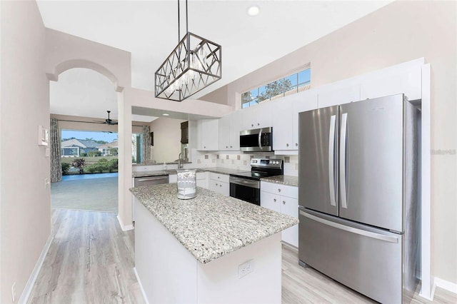 kitchen featuring tasteful backsplash, stainless steel appliances, white cabinets, pendant lighting, and a kitchen island