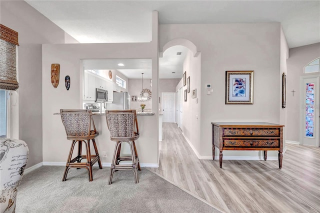 interior space with appliances with stainless steel finishes, light hardwood / wood-style flooring, a breakfast bar area, white cabinetry, and kitchen peninsula