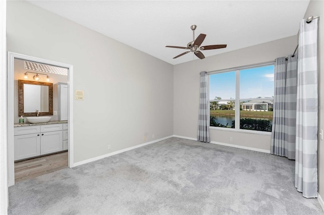 unfurnished bedroom with light carpet, a water view, sink, and connected bathroom