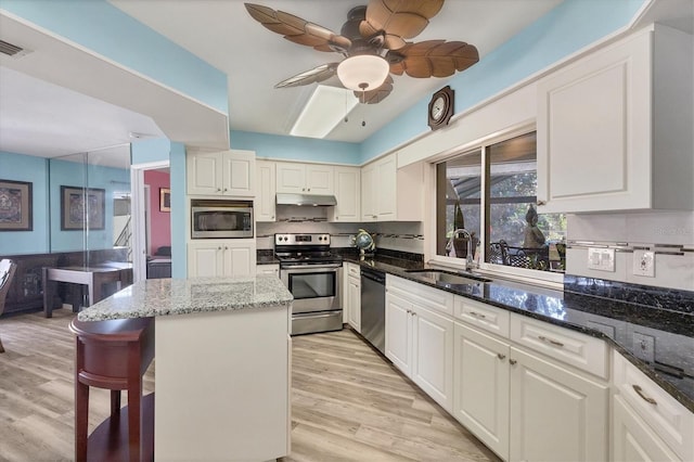 kitchen with white cabinetry, sink, stainless steel appliances, dark stone counters, and light wood-type flooring