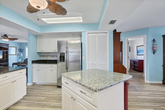 kitchen with light wood-type flooring, dark stone countertops, white cabinets, stainless steel fridge with ice dispenser, and a center island